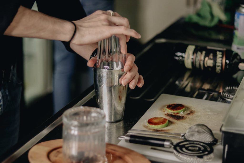 pexels photo 16043263 Close-up of a bartender using a shaker to mix a cocktail in a kitchen setting.