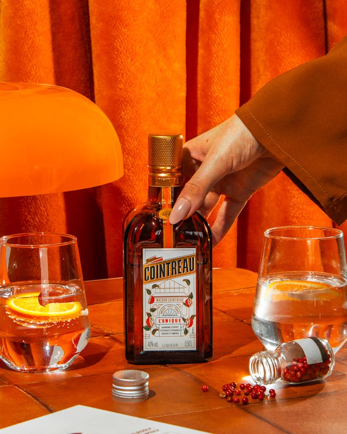 Vibrant setup featuring Cointreau bottle and citrus cocktail on an orange background.